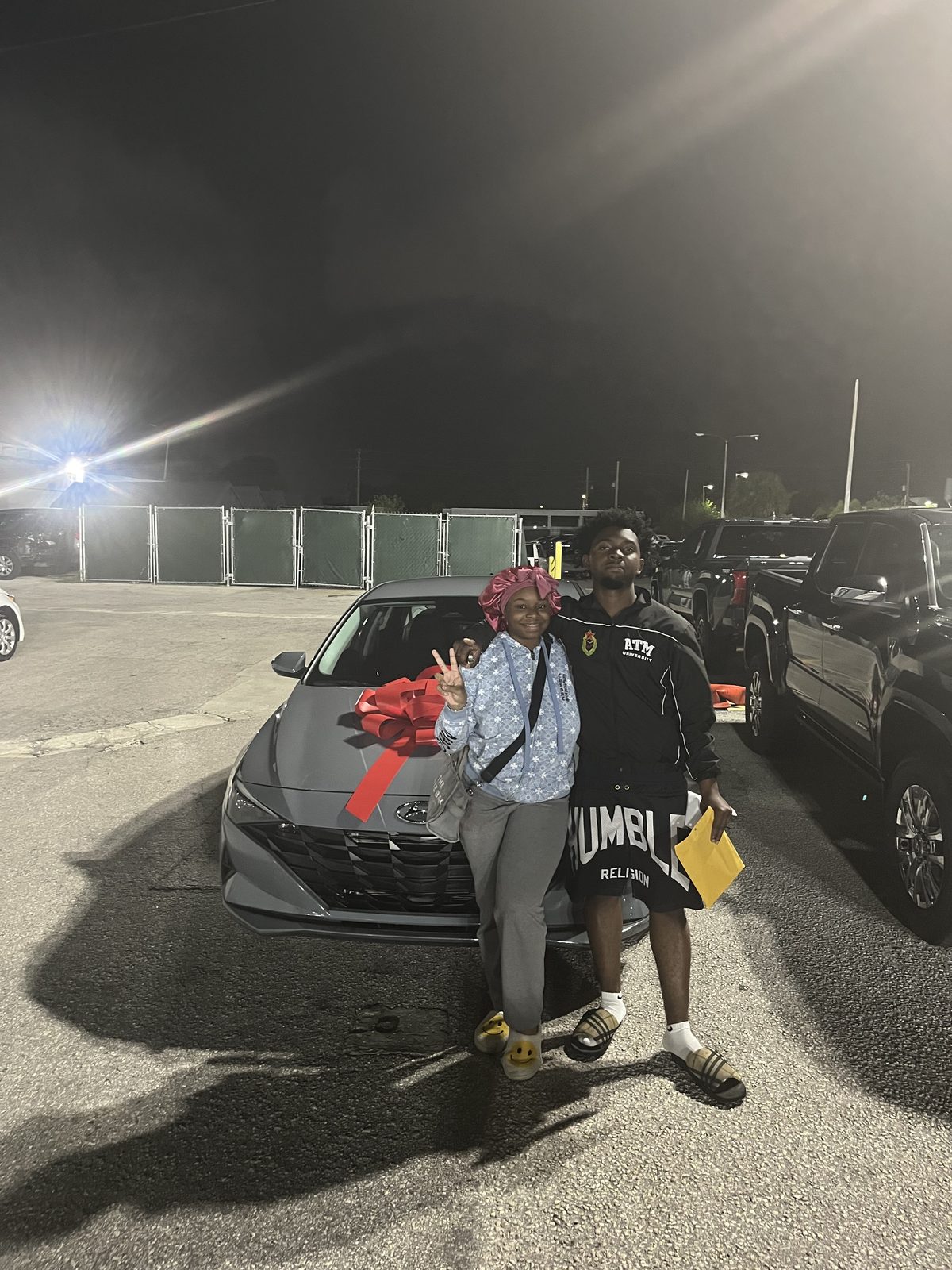 Customer with a new grey sedan wrapped in a red bow at night.