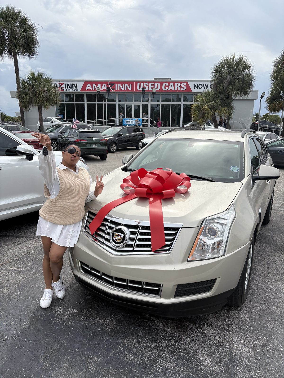 Customer holding up keys beside a cream SUV with a red bow in a dealership lot.